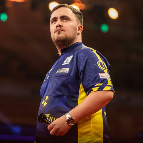 Darts player Luke Littler in a blue and yellow shirt, holding darts, looking up intently.