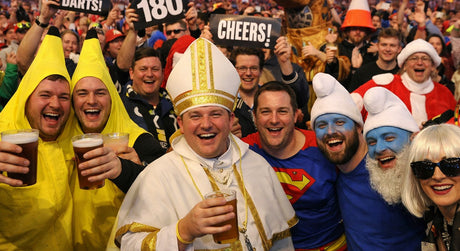 Smiling darts fans in costumes, including a pope, bananas, Superman, and Smurfs, holding beers.