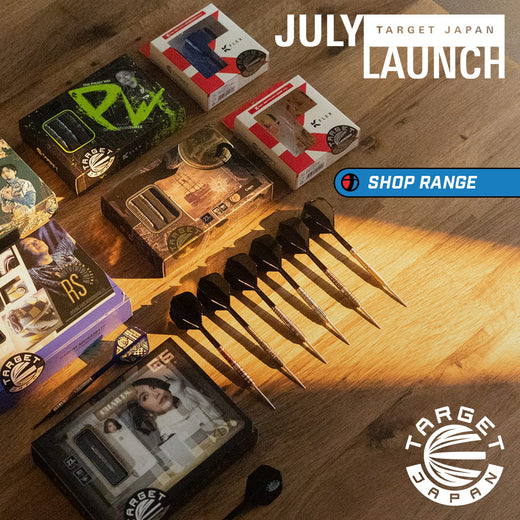 Target Japan July Launch promotional display featuring a set of black and silver darts arranged on a wooden surface with multiple branded product boxes around them. Promotional text reads 'JULY TARGET JAPAN LAUNCH' and 'SHOP RANGE', with Target Japan branding visible.